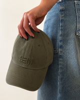 Person holding a green cap with 'Sena' branding against a light background